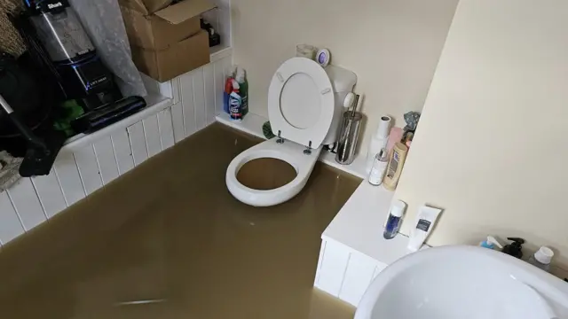 A bathroom flooded with brown water up to the toilet seat