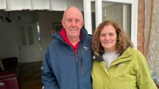 A couple stand in front of their flooded home.