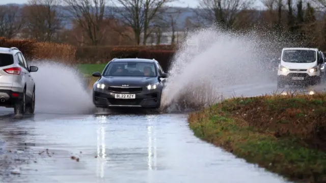 Vehicles driven through a flooded road in Aldingbourne, West Sussex