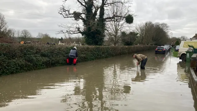 People attempting to unblock drains on a flooded road