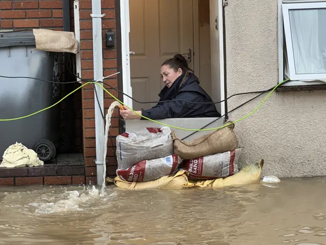 Woman empties water out of her home in Alney Island, Gloucestershire