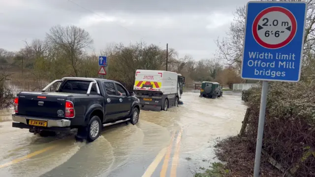 Vehicles pass through a flooded street after heavy rain in Cambridgeshire