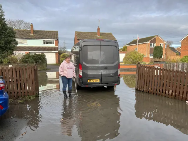 Woman in front of van parked on flooded road