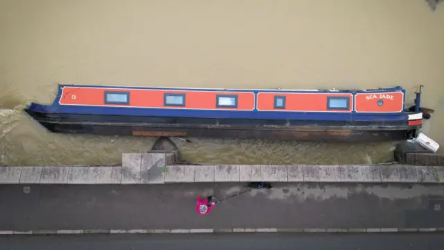 A dog walker passes an overturned narrowboat in the River Soar, Leicestershire