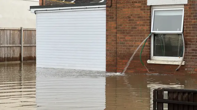 Garden houses being used to empty water out of a house through a window in Longford, Gloucestershire