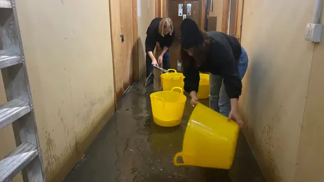 Two women with buckets removing water from a hallway.