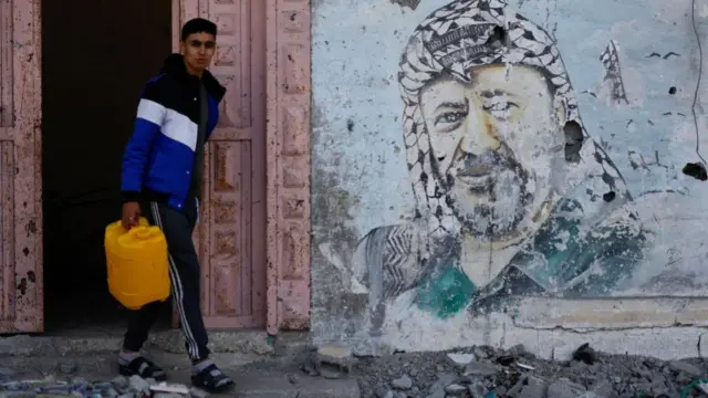 A Palestinian carries a container near the rubble of a house destroyed in an Israeli strike, in Rafah