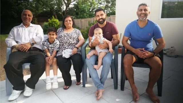 The family sit in the back garden, smiling at the camera