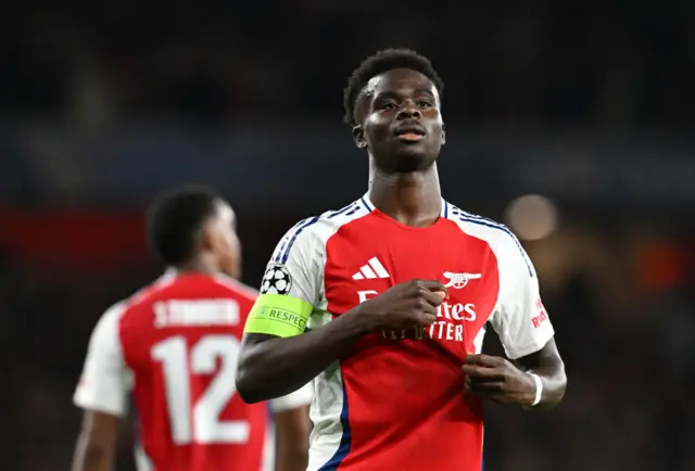 Saka pats the badge on his shirt to celebrate his goal