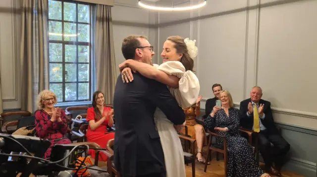 Oliver and Georgina embrace in front of beaming guests at the town hall