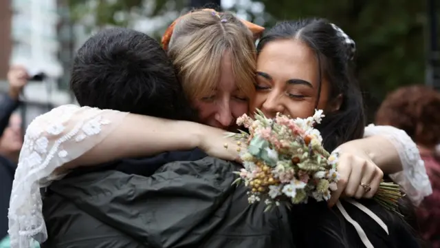 Bridge Samantha Jamieson Green hugs her niece and nephew. She is holding a bouquet in one hand.