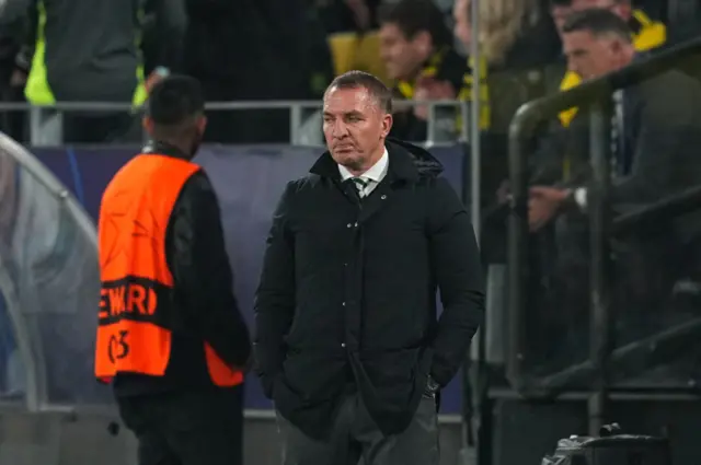 Rodgers stands with his hands in his pockets on the touchline