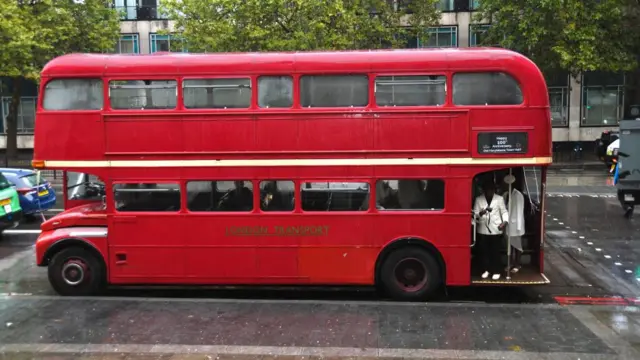 A wedding party shelters on a 100 anniversary wedding bus outside Old Marylebone Town Hall