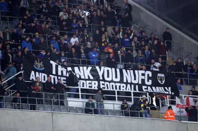 Fans of AFC Wimbledon display a banner thanking Newcastle United football club