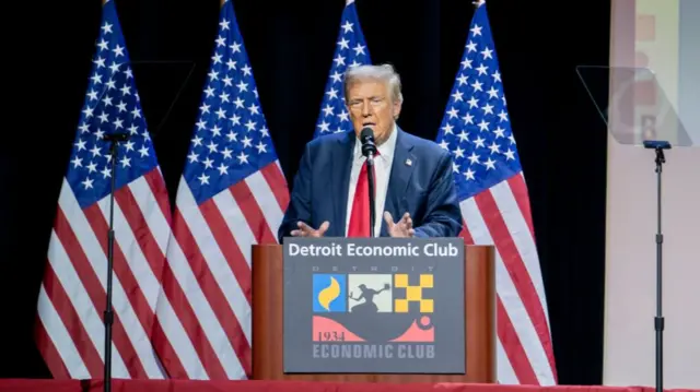 Donald Trump stands in front of a row of American flags