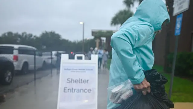 A person carrying a large bag heading towards a shelter, with a large white sign saying "Shelter Entrance"