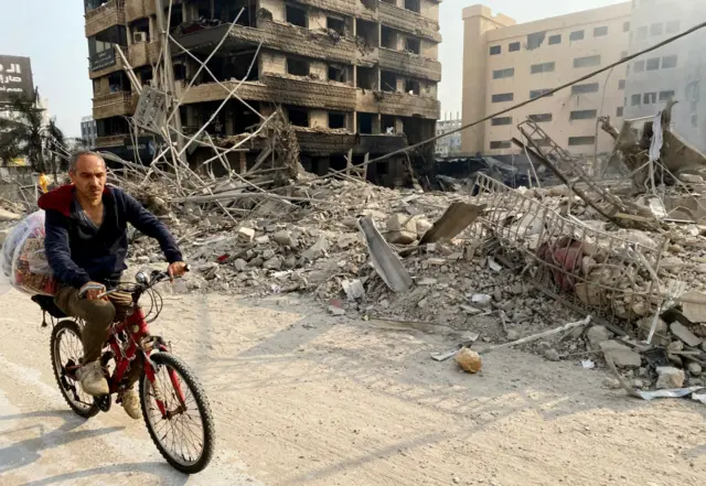 A man cycles past a destroyed building