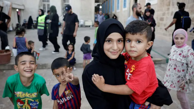 Children pose in a school turned into a temporary shelter for displaced people, during a visit by Hezbollah members of parliament,