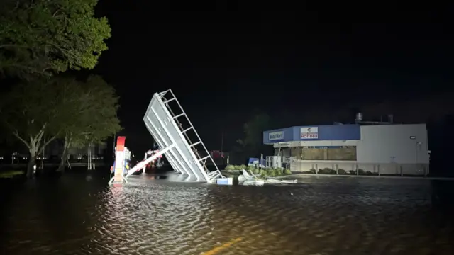 A petrol station shelter on its side after falling down during Hurricane Milton. To the right of the image you can see the shop, which is white and blue.