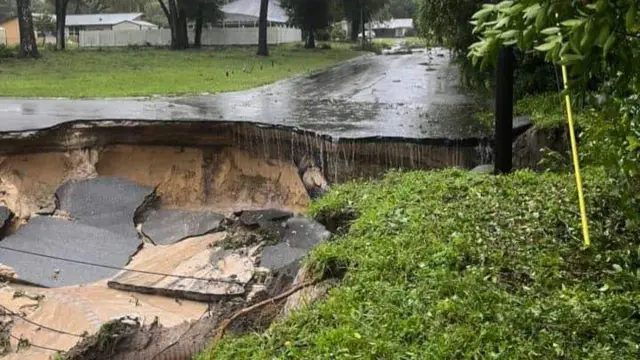 Sections of tarmac crumbled into the ground with mud and rainwater streaming on top of it