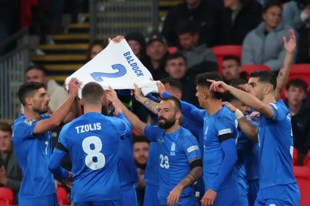 Greece players hold up Baldock shirt in tribute