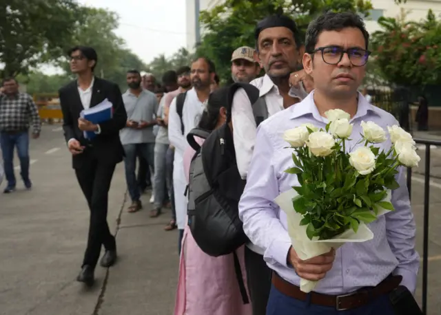 A man holding flowers waits in a queue outside the National Centre for the Performing Arts (NCPA), to pay their respects to Ratan Tata.