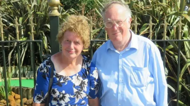 Lois and John McCullough, who are standing in front of a mini golf course. They are both dressed in blue and smiling at the camera.