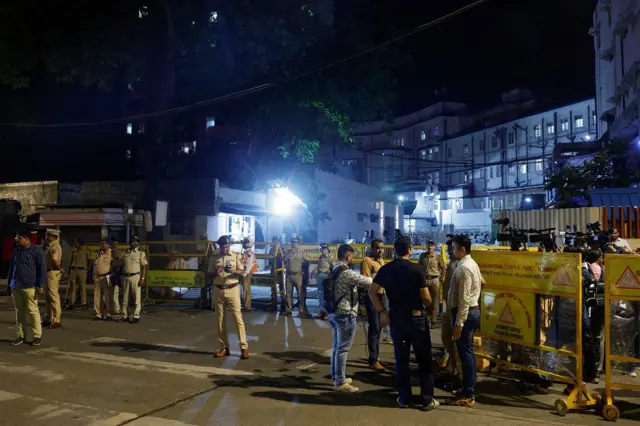 Law enforcement officers stand guard as media wait outside a hospital where former chairman of Tata Group, Ratan Tata passed away in Mumbai