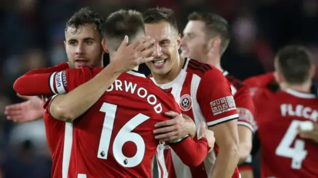 George Baldock hugs Sheffield United team-mate Ollie Norwood with Phil Jagielka smiling in the background