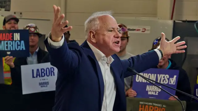 Tim Walz stretches out both arms as he talks to a crowd