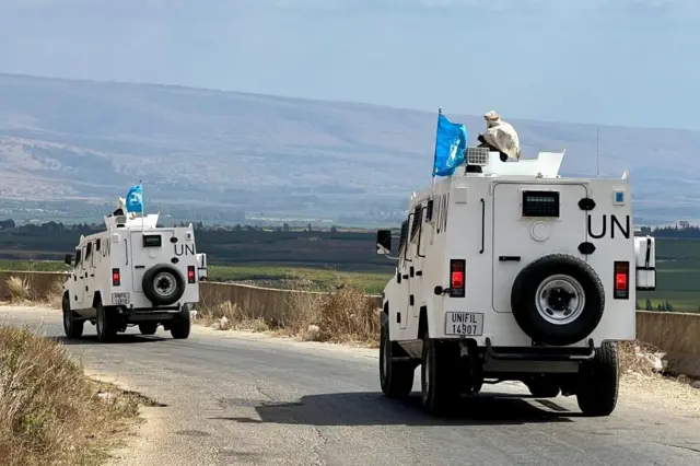 Two white trucked marked with large UN signs and blue flags patrol Wazzani village in southern Lebanon with view of mountains in background