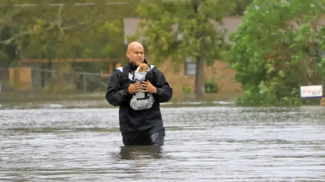 A man carrying a dog moves through floodwaters in South Daytona, Florida after Hurricane Milton.