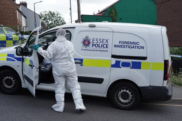 A white Essex Police forensic investigation van with an officer in a white protective suit with his hand on the open passenger door.