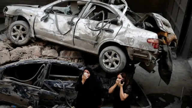 Women stand next to damaged vehicles at the site of an Israeli air strike, amid ongoing hostilities between Hezbollah and Israeli forces, in Beirut, Lebanon, October 11, 2024.