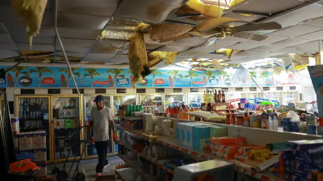 A man walks through a store that has been damaged by the hurricane. Insulation is galling out the ceiling, and it is water damaged.