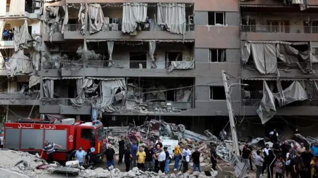 An emergency service vehicle and a group of individuals can be seen against the backdrop of a damaged buidling and rubble on the floor