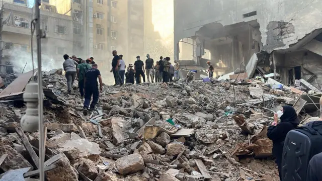 A group of men atop a pile of rubble in Beirut, assessing the damage of an Israeli airstrike.