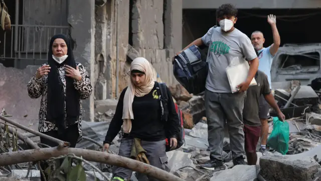 People hold their belongings as they walk among the rubble