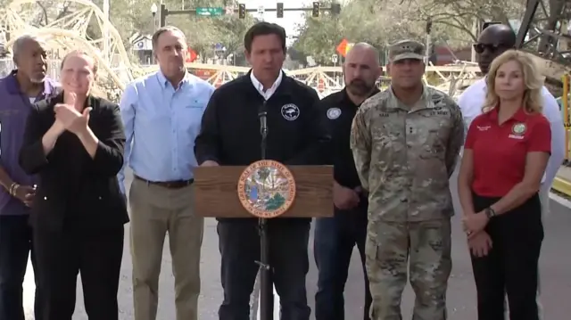 Ron DeSantis speaking at a lectern with people surrounding him