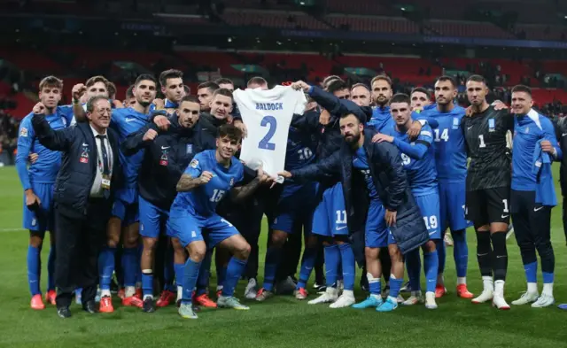 Greece's players hold up George Baldock's shirt after beating England at Wembley