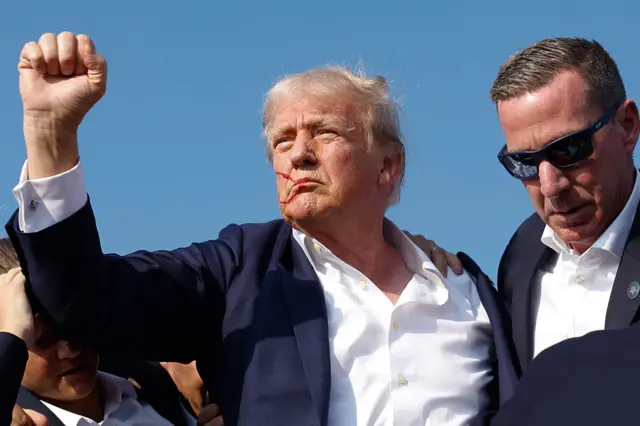 Republican presidential candidate former President Donald Trump pumps his fist as he is rushed offstage by U.S. Secret Service agents after being grazed by a bullet during a rally on July 13, 2024 in Butler, Pennsylvania