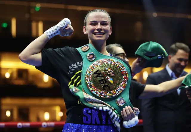 Skye Nicolson holds up her fist and is wearing the WBC featherweight title over her shoulder