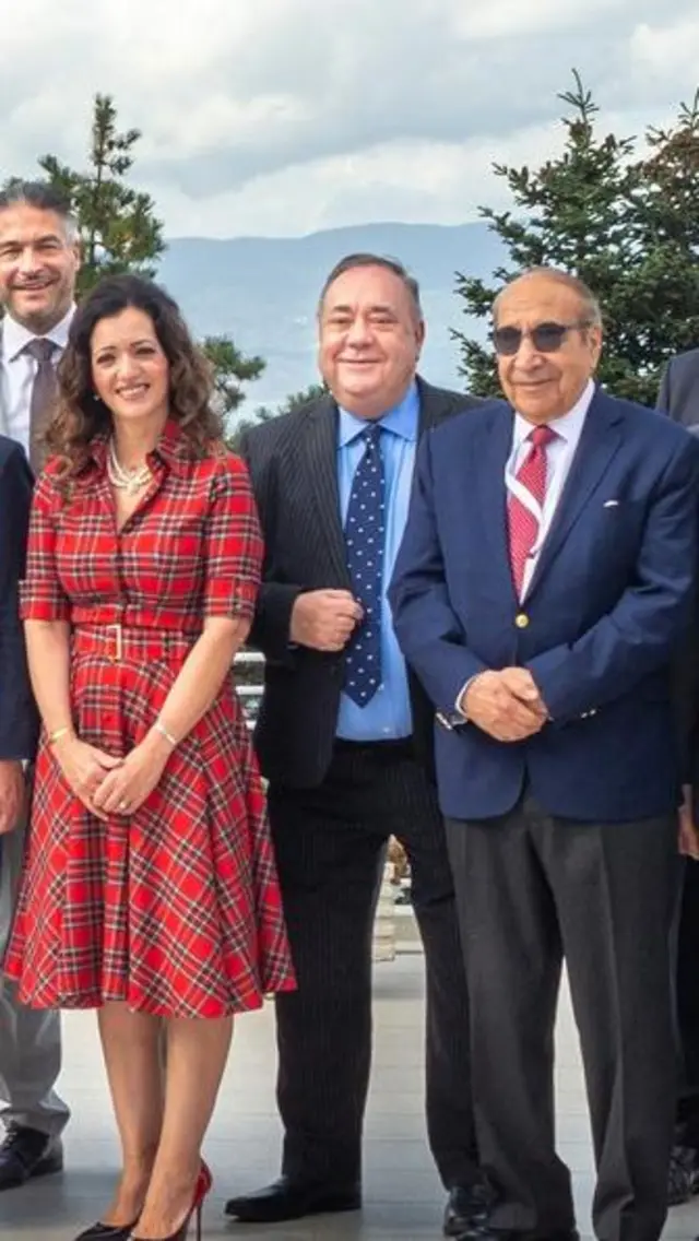 Nineteen people, including Alex Salmond, stand in a row in business-wear posing for a group photo