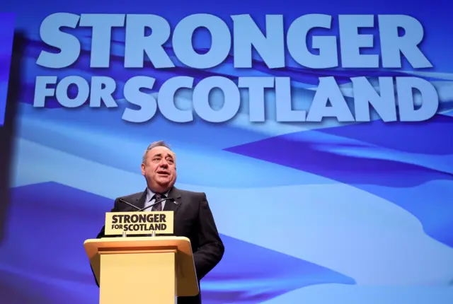 Alex Salmond stands behind podium which reads: "Stronger for Scotland". Behind him a giant Scotland flag is projected on to a screen with the words "Stronger for Scotland" written on top