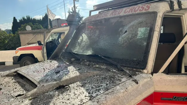 Close up of the front of a Lebanese Red Cross ambulance with rubble on the front hood and damaged frontscreen