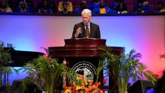 Bill Clinton standing at a podium with congregants of the church sitting in a row behind him