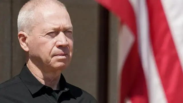 Israeli Defence Minister Yoav Gallant in close-up, with a flag to his right