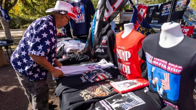 A man, wearing a cowboy hat and starry shirt, folds pro-Trump T-shirts