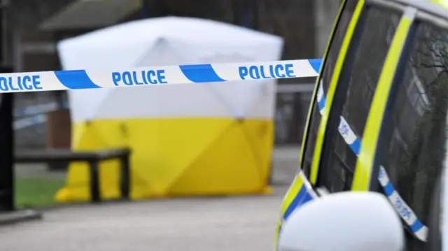 A police car is parked next to crime scene tape, as a tent covers a park bench on which former Russian inteligence officer Sergei Skripal, and a woman were found unconscious after they had been exposed to an unknown substance, in Salisbury