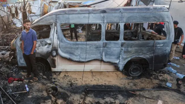 A man stands beside the remains of a vehicle following strikes at the al-Aqsa Martyrs Hospital in central Gaza